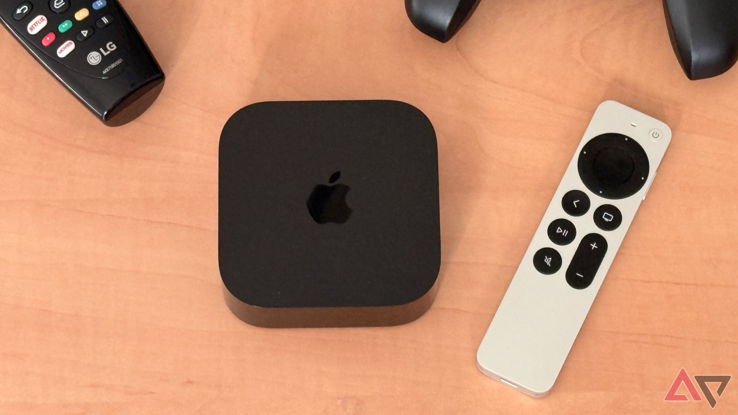 Apple TV 4K на легкому дерев’яному столі з пультом Siri Remote, LG TV Remote та Nimbus Game Controller