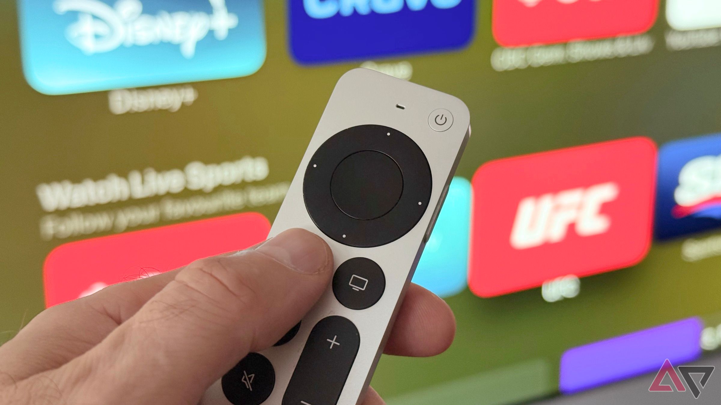 Рука, що тримає дистанційну пульт Siri перед екраном Apple TV