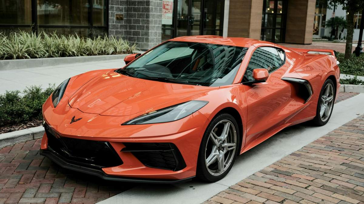 2025 помаранчевий Corvette C8, припаркований на цегляній доріжці, демонструючи свій сучасний дизайн та спортивні особливості в міській обстановці.