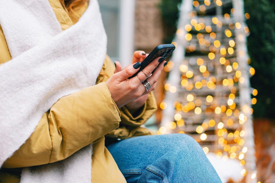 Жінка за допомогою смартфона на відкритому повітрі під час зими біля ялинки